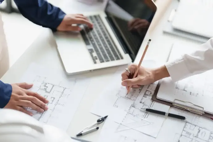 Architecte travaillant sur un plan à côté d'un ordinateur